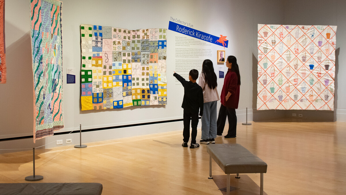 A woman, girl and boy look at a colorful quilt in an International Quilt Museum gallery. There is text next to the quilt with the header "The Collector's Eye: Roderick Kiracofe."