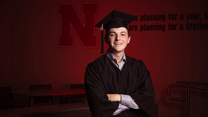 Business student Caleb Newburn stands, arms crossed, by a Hawks Hall wall decorated with the Nebraska N.