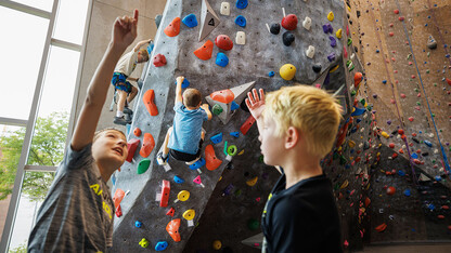 Campers discuss their strategy in front of the rock climbing wall as others take on the climbing the wall.