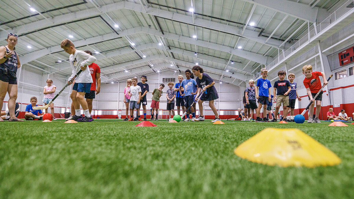 Children try out hockey equipment on a green turf inside the Campus Recreation Center.