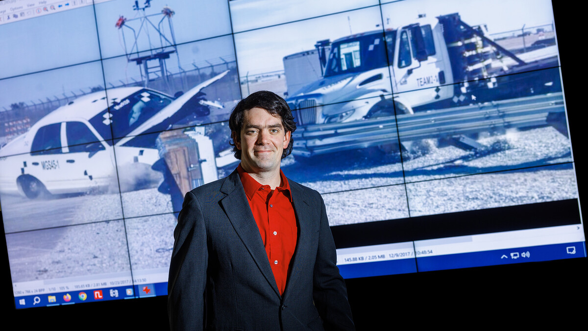 Cody Stolle posed in front of crash video footage from testing done at the UNL Midwest Roadside Safety Facility.