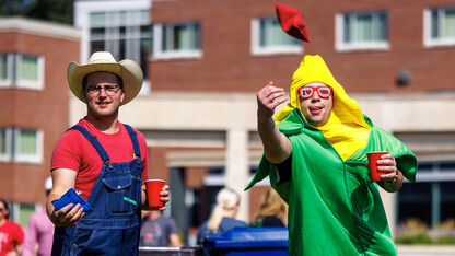 Students, one dressed like a farmer, the other like an ear of corn, compete in a bean bag toss during a campus tailgate in 2023.