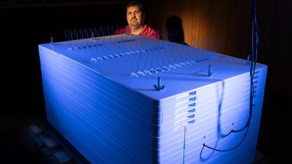 Trenton Franz with a neutron monitor.  The sensors are housed in the box surrounded by lead bricks which is surrounded by plastic. The monitor sits in an unused lunchroom inside an old munitions building at the Eastern Nebraska Research, Extension and Education Center (ENREEC) near Mead, Nebraska. Franz, associate professor Assoc Professor in the School of Natural Resources, is using neutron and cosmic ray detectors to see how solar radiation and solar energy such as those that caused Nebraksa t