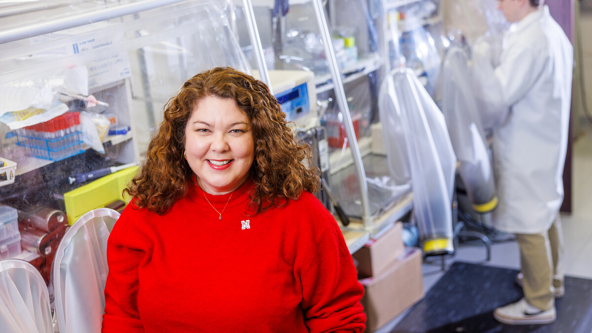 Dr. Nicole Buan sits on the left side of the frame in a red sweater, in front of a lab.
