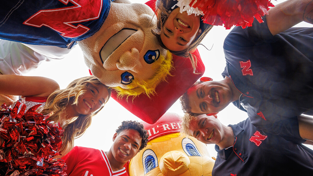 Aidan Kauth Fisher, a CEHS major who worked as Lil Red, Connor Hadaway, a Child Youth and Family Studies major who worked as Herbie in his undergrad, Amani Mfinanga, a senior Management major and Nebraska Spirit Squad member, Kylie Jones, a senior Marketing major and member of the Husker Scarlets and Grace Nab, a senior Nutritional Science and Dietetics major and member of the Nebraska Spirit Squad pose for a photo with Lil Red and Herbie on the turf in Memorial Stadium for their graduation.