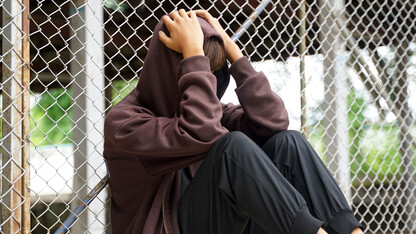 A teen sits against a fence.