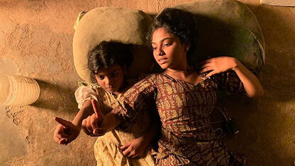 Two little girls with brown skin and dark hair lay next to each other with their hands in the air.