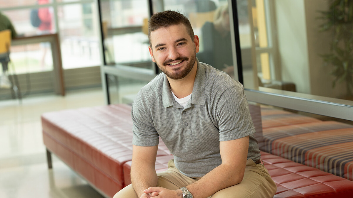 Baden Brumbaugh sits in a grey shirt and khakis, with his hands together and with short brown hair and a beard.