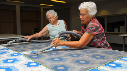 Museum volunteers vacuum dust from a quilt. Screens are used to protect the quilt during the process.