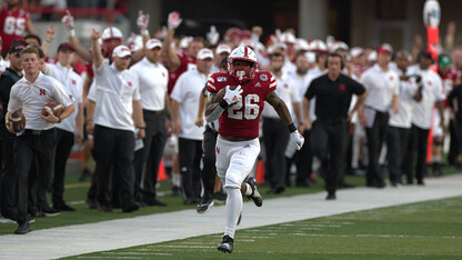 With the team bench celebrating in the background, Nebraska's Dedrick Mill surges down the sideline for a touchdown in Memorial Stadium. Mills recently cataloged his journey, highlighting his struggles and recent successes realized through supports at Nebraska. The story was featured in the Huskers' "N" Our Voice series.