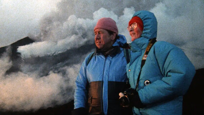 Katia and Maurice Kraff, who are featured in “Fire of Love,” stand with steam from a volcano in the background.
