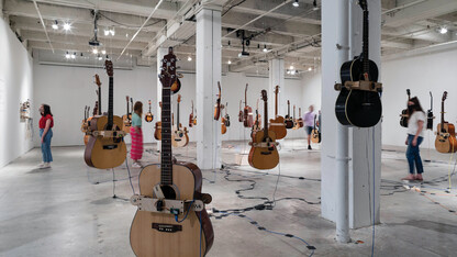 Guitars hang in the air as patrons examine the "Soundtracks for the Present Future" exhibition in Omaha's Bemis Center for Contemporary Arts.