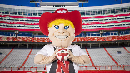 Herbie Husker stands in Memorial Stadium holding a volleyball.