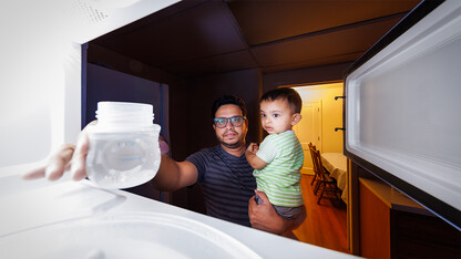 Kazi Albab Hussain holds his son while removing a plastic container from a microwave