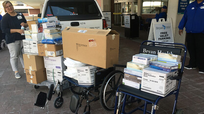 Bryan Health workers load supplies from Jessica Corman's truck into a pair of wheelchairs. The supplies were donated by campus labs.