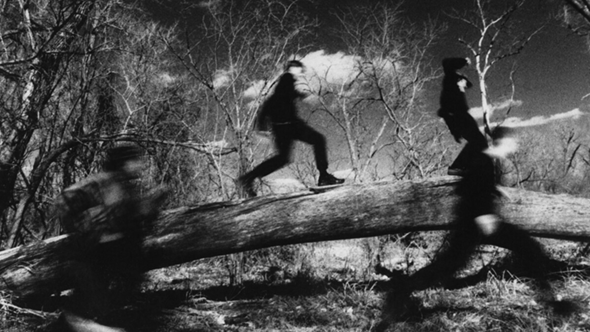 A black and white photo of four dark, blurry figures running through a forest.