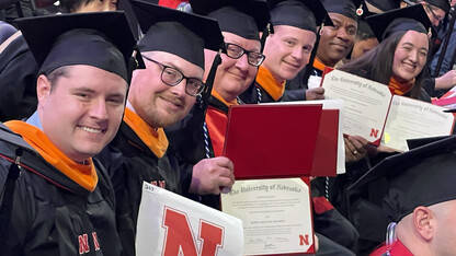 Master of Engineering Management graduates sitting in a row while wearing regalia hold up their diplomas during commencement exercises in December 2024.