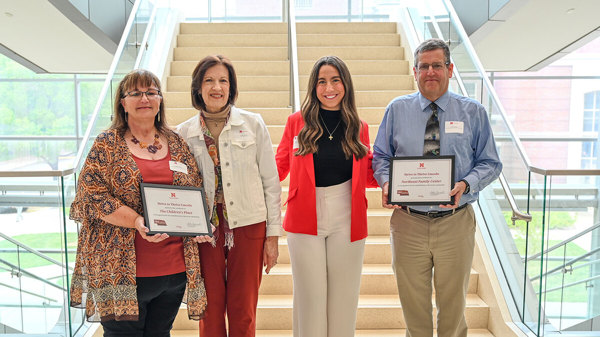 Kathy Majors in a red shirt and patterned cardigan with red hair and glasses, who holds a certificate, Kathy Paisley in red pants and a white jean jacket with short brown hair, Nikoleta Skoufis in white pants, a black turtleneck and a red blazer with long brown hair, and Curt Krueger in khakis, a blue shirt and tie and glasses, holding a certificate.