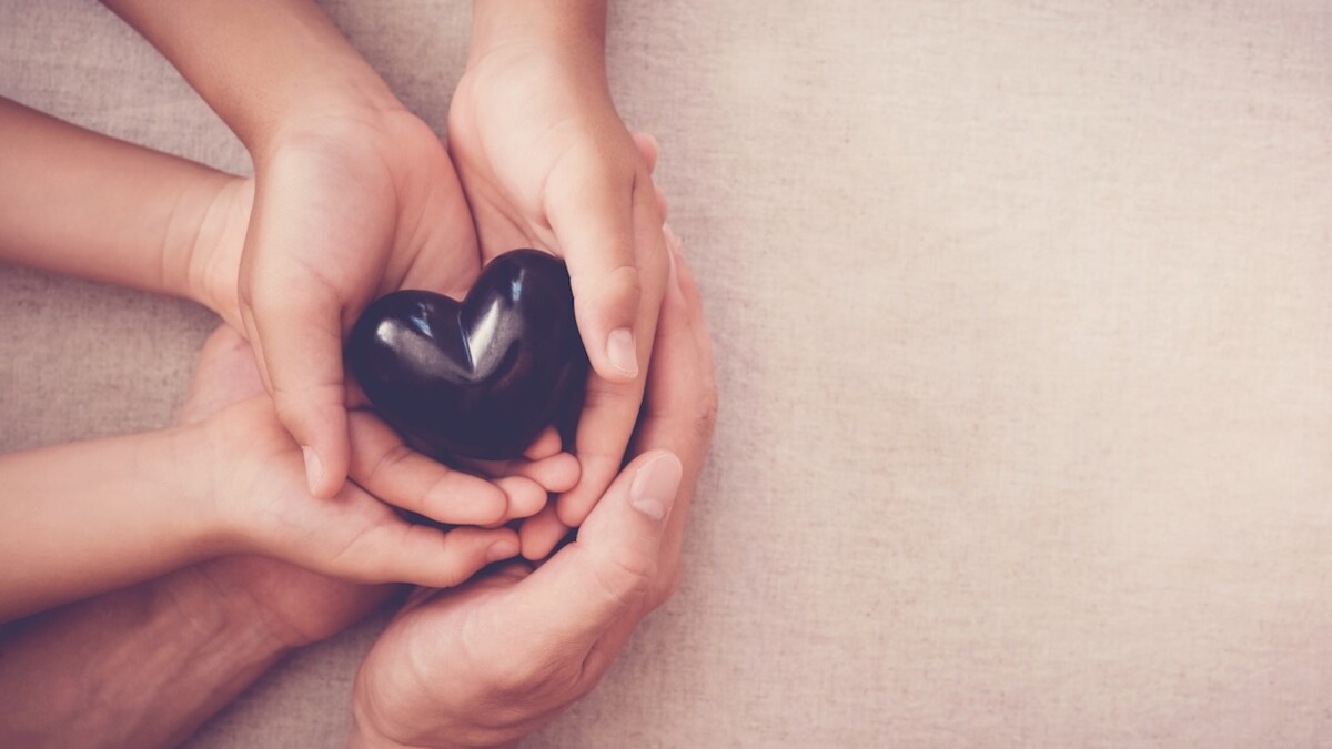 multiple hands clasped together, holding a black heart