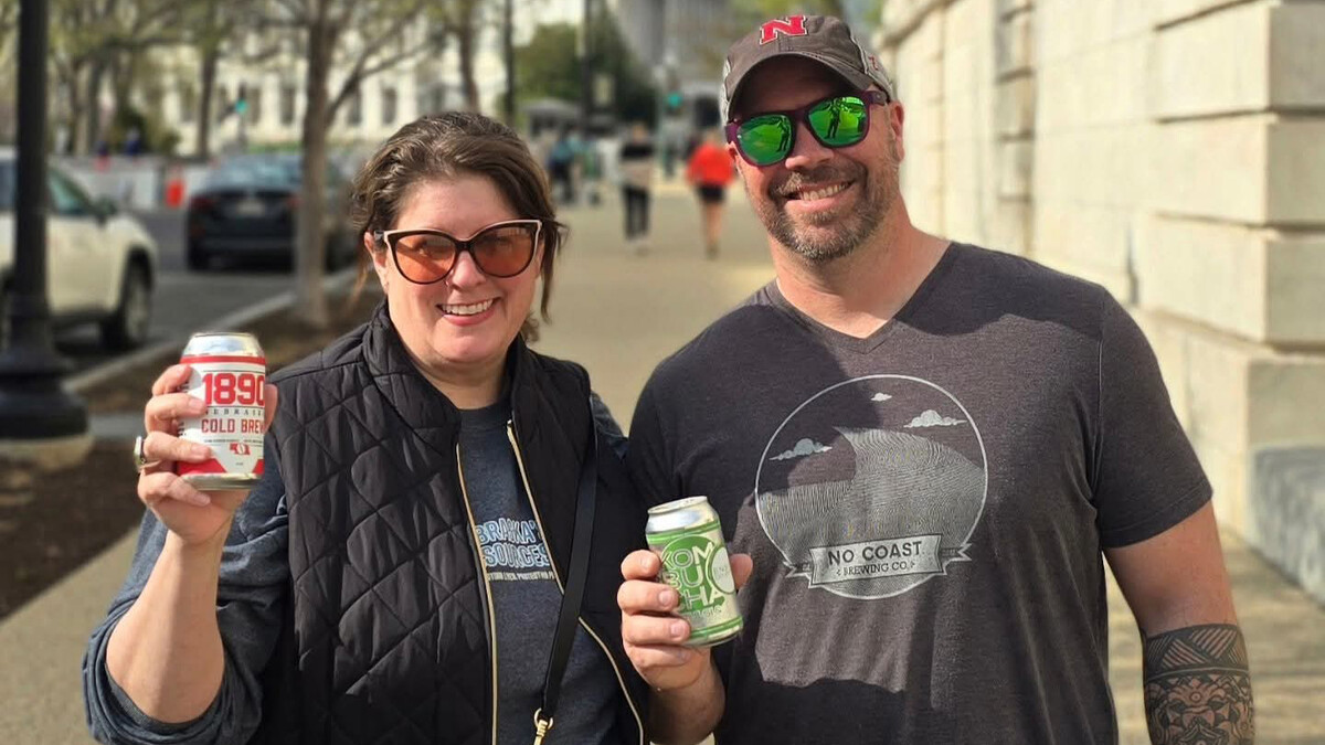 Two people hold up cans facing the camera.