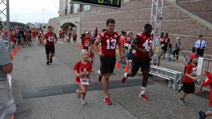 Huskers run alongside participants outside of Memorial Stadium in the Nebraska Football Road Race.