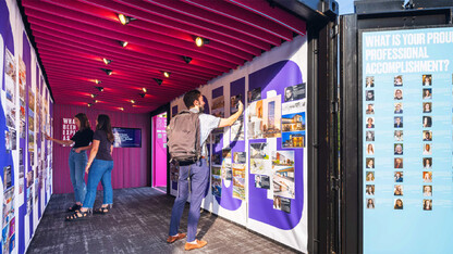 Rendering showing the interior of the Say It Loud exhibition, which is inside a converted shipping container. Image shows three people reading about individuals featured in the exhibition.