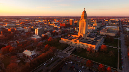 Nebraska State Capitol building and fall trees lit up red by a setting sun.