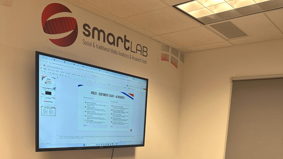 A white wall with the words "SMART Lab" depicted above a tv showing slides about the SMART Lab.