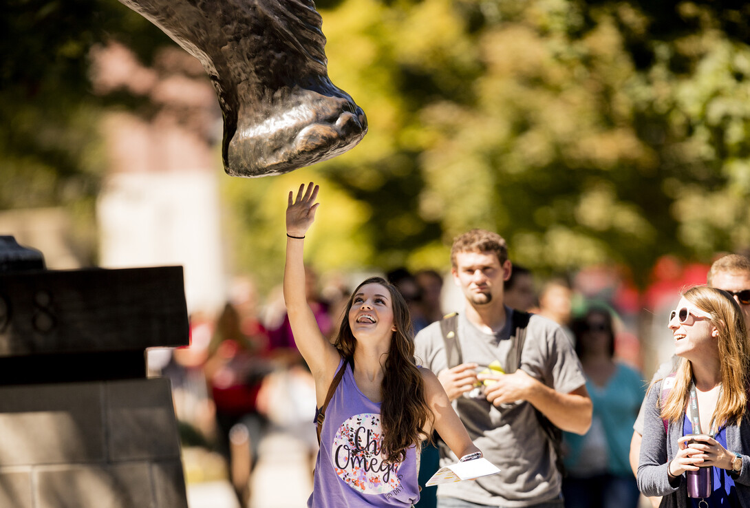 A Nebraska student reaches up to give the Archie sculpture a high-five. Campus legend claims that a high-five from the mammoth brings good luck.