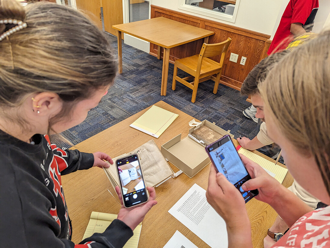 Students take photos of a medieval manuscript.