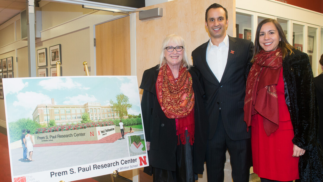 Members of Prem S. Paul's family stand next to a architectural drawing of new signage that will be installed on the south side of the recently renamed Prem S. Paul Research Center at Whittier School. Pictured (from left) is Prem’s widow, Missi Paul; son Ryan Paul; and daughter Neena Paul.
