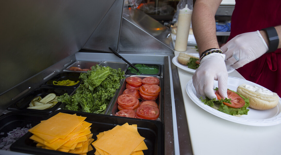.A housing employee builds a bacon ranch burger for a customer. Burger recipes change with each summer barbecue event.
