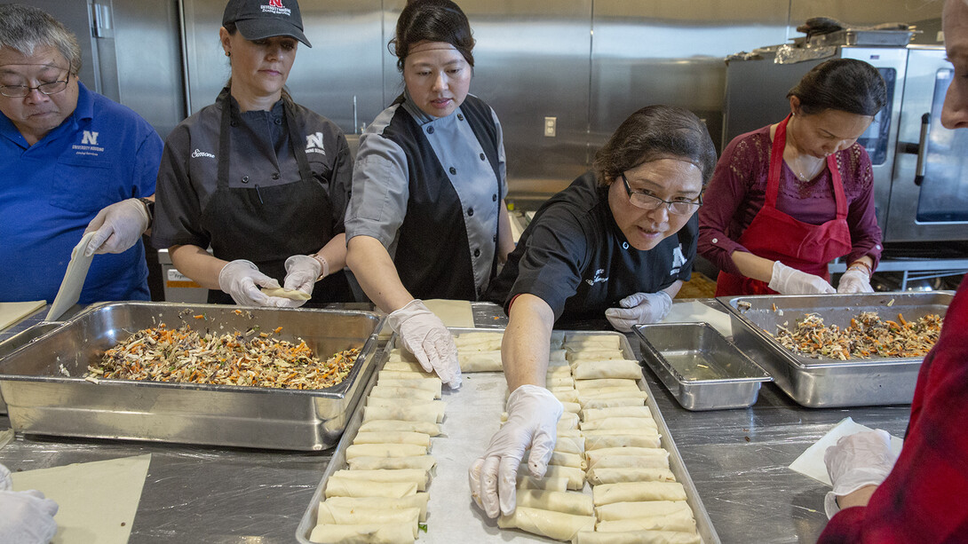 Thom “Emily” Tran (third from left) and Amy Tran (fourth from left) adjust raw egg rolls on a baking sheet in the Cather Dining Center on Jan. 9. For the second year, Cather Dining Center is offering handmade vegetarian egg rolls based on a recipe provided by Tran. The homemade option has proven popular with students and is healthier and cheaper than purchasing a frozen option.