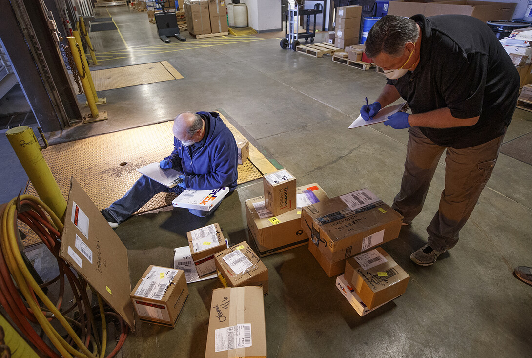 Pat Huberty (from left) and Ed Kerney check in and sort packages following a FedEx delivery. Package delivery has been consolidated at the Facilities Management Shops on north 22nd St. There, the packages are sorted, logged in and the recipients notified to pick up the package or have it stored until they return.