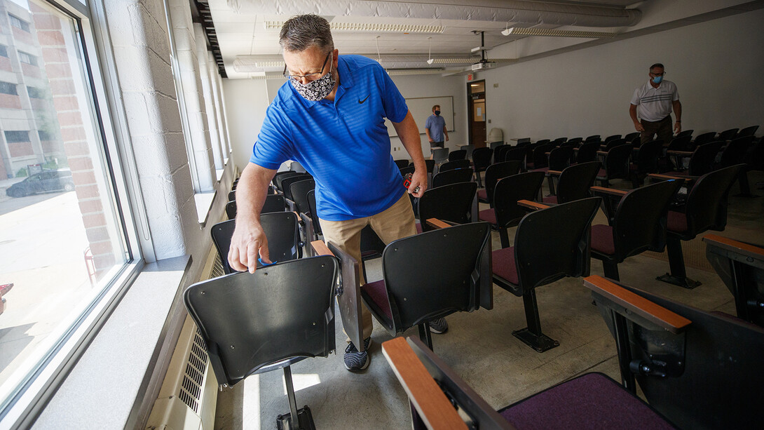 Shawn Languis places tape on the back of a chair that will be unavailable due to six-foot social distancing guidelines. The group is physically measuring every classroom on campus to see if computer-aided predictions are correct.
