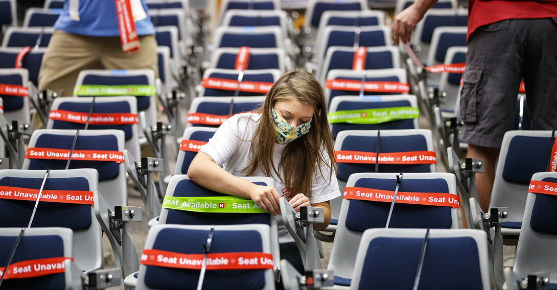 Maddie Huppert, a student worker in the Office of the Executive Vice Chancellor, wraps a green band on an available seat in a Louise Pound Hall lecture space. The bands are flexible so they do not need to be removed when the student sits down.
