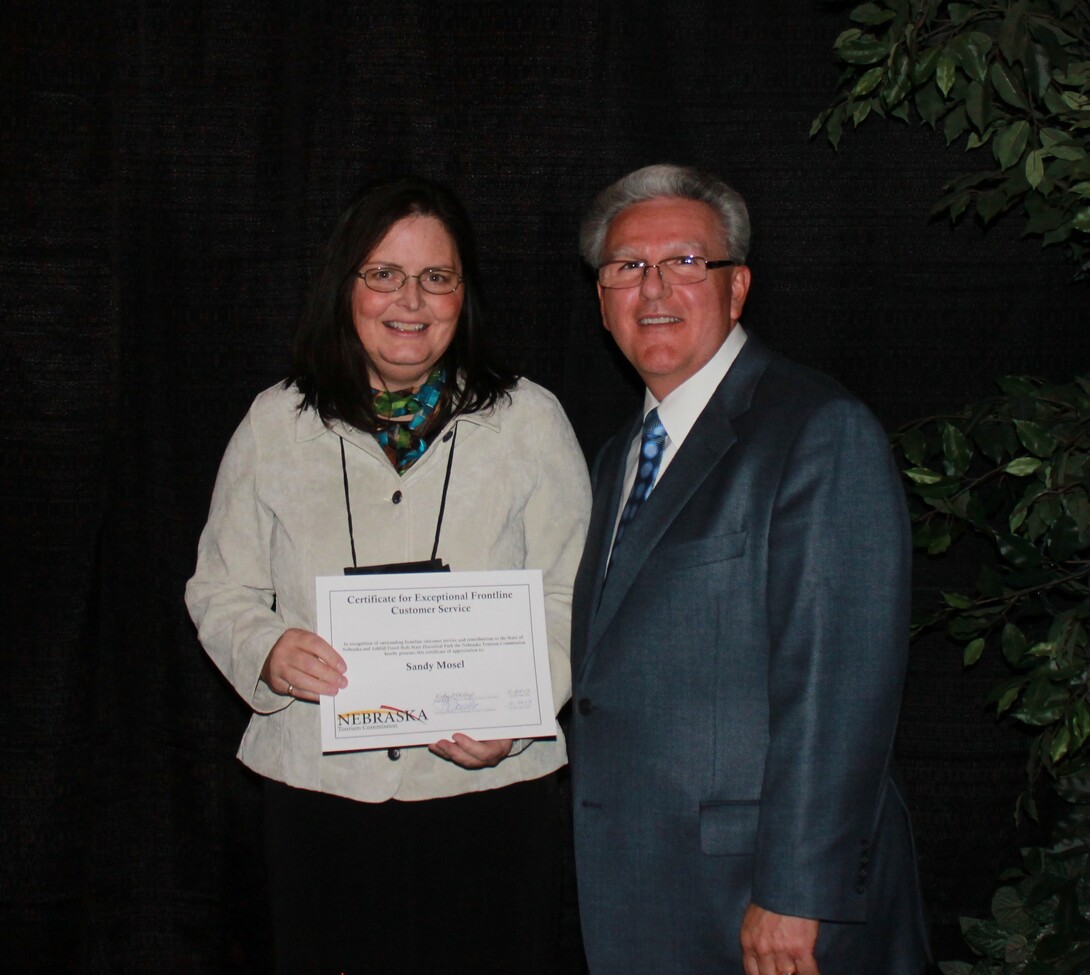 Senator Jim Scheer presents Ashfall’s Sandy Mosel with the Exceptional Frontline Customer Service certificate from the Nebraska Tourism Commission.