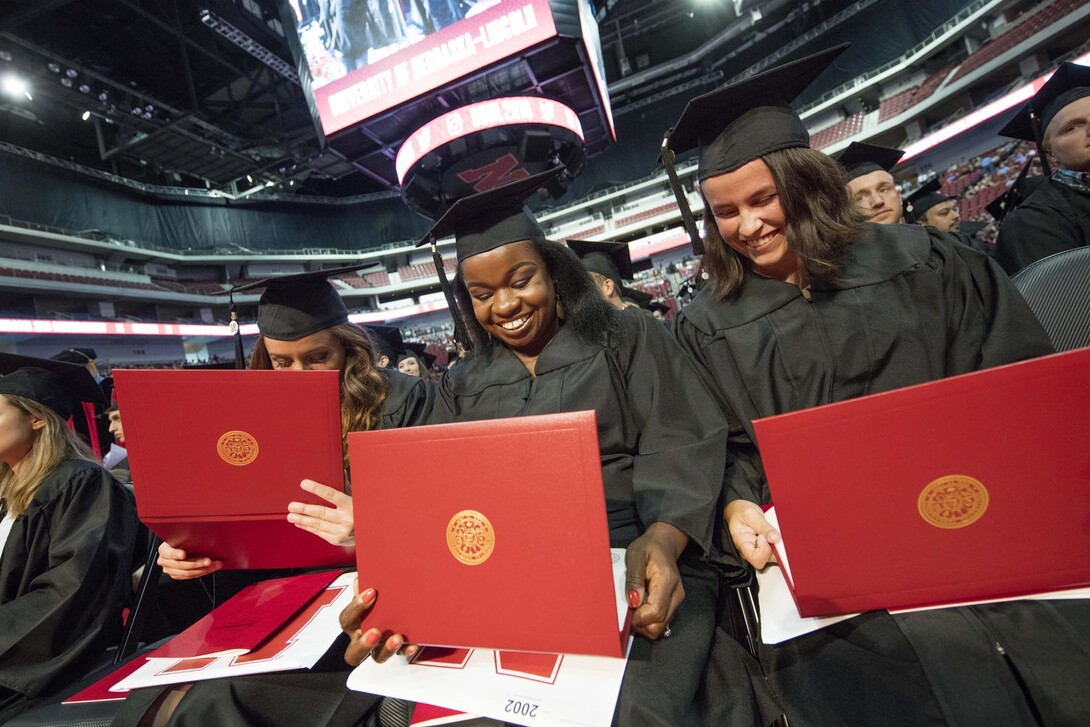 (From left) Julia Storm, Davetta Nelson and Gianna Astorino look over their diplomas in criminal justice during the summer all-university commencement ceremony Aug. 13 at Pinnacle Bank Arena.