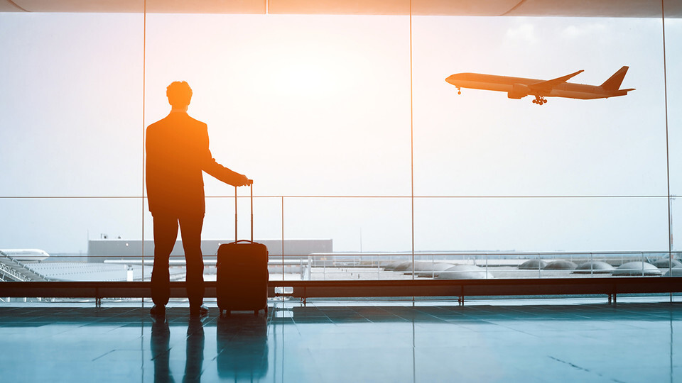 Silhouette of a man standing in airport, hand on suitcase, watching an airplane land.