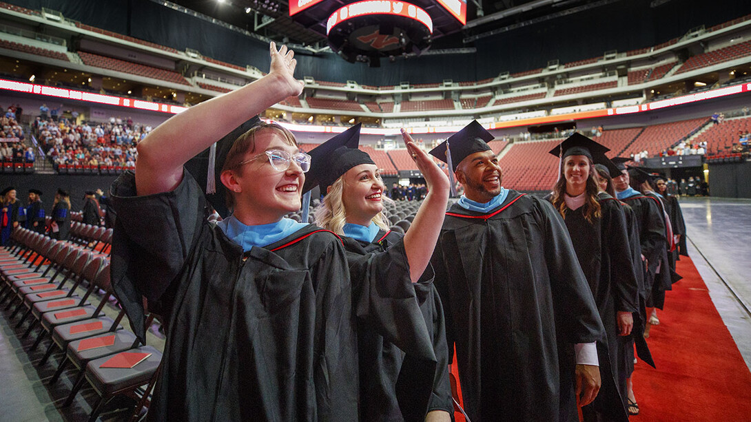 (From left) Maggie Fischer, Natalie Floreani and Phillip Foster wave to the crowd as they enter Pinnacle Bank Arena for the graduate and professional degrees ceremony May 4.