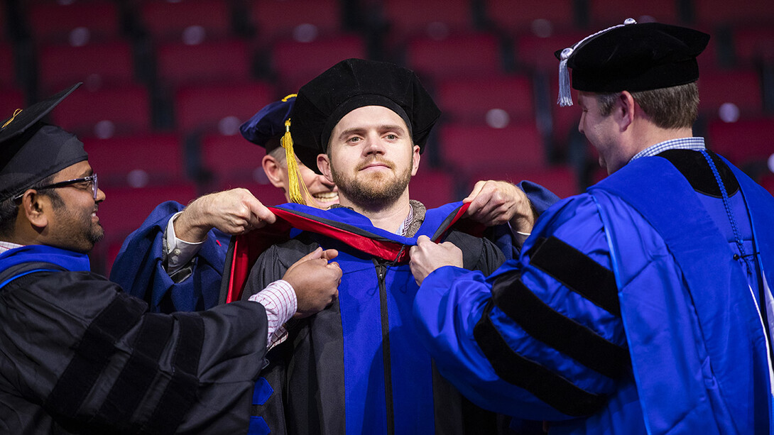 John Evans IV has his doctoral hood placed over his head by professors Santosh Pitla and Joe Luck during the graduate and professional degree ceremony Dec. 14 at Pinnacle Bank Arena. Evans earned a Doctor of Philosophy in biological engineering.
