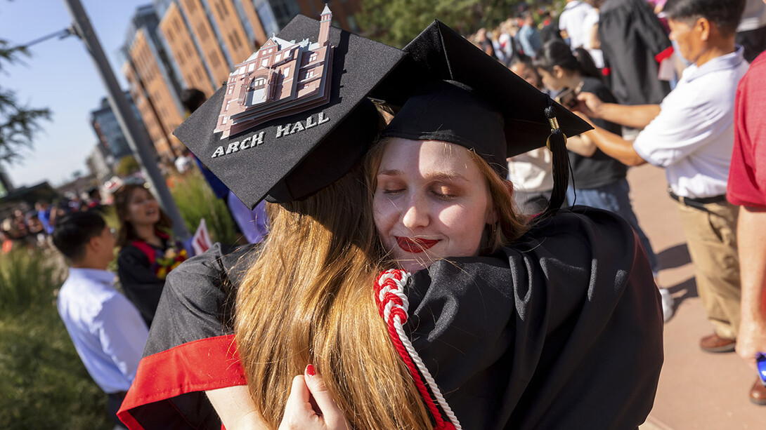 Leia Farrens and Margaret Gies, 2020 architecture graduates, hug after the undergraduate commencement ceremony Aug. 14 at Pinnacle Bank Arena. Gies decorated her mortar board with a rendering of Architecture Hall.