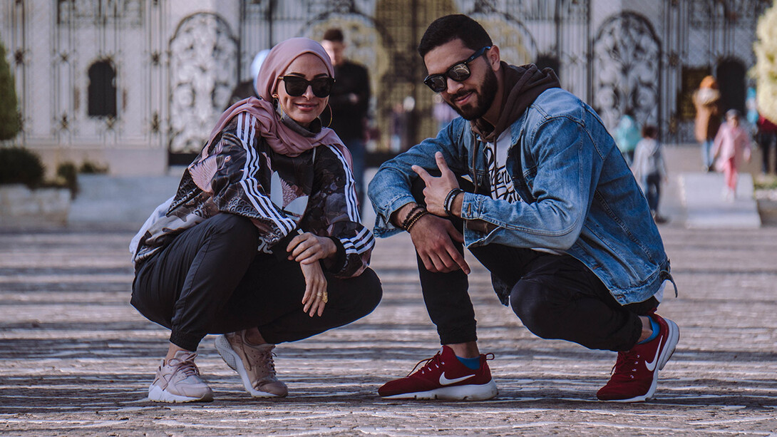 Amirah Sackett and MR MiC crouch near the ground, wearing sunglasses and hip-hop attire