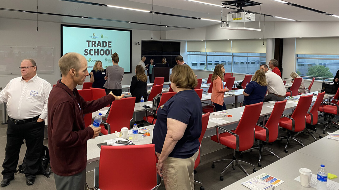 Fifteen or so people chat in a meeting room with "Trade School" projected on a screen in front.