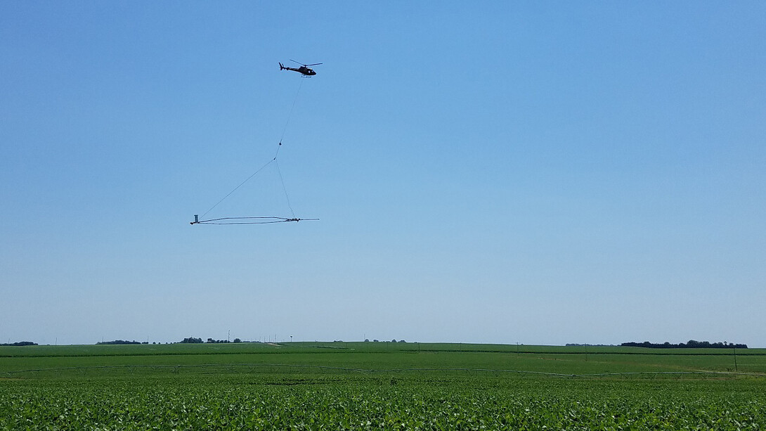 A helicopter carries a large loop of wire whose electromagnetic signaling enables extensive imagery of subsurface conditions and the creation of a 3D geological model.