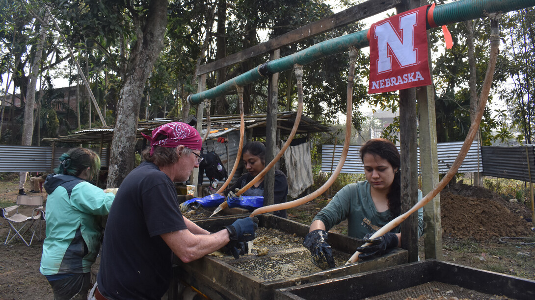 Four people wet-screen sediment in search of material.