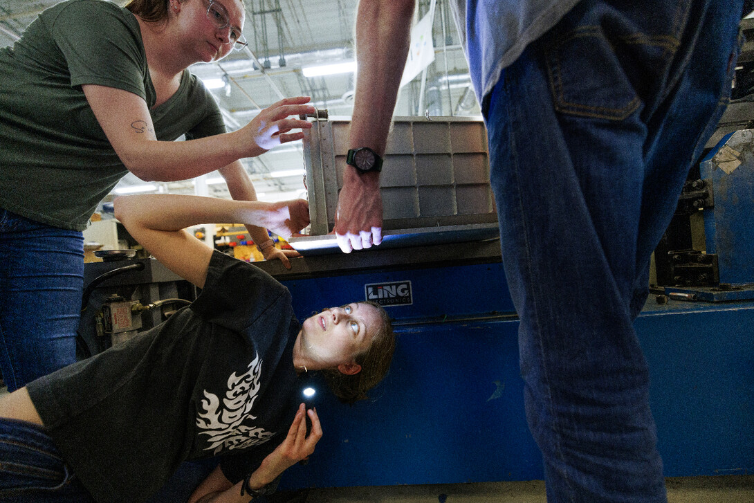  Rachael Wagner, a Husker graduate and Virtual Incision employee, aligns the holes in a plate to bolt the robot case onto the shake table as Erika Smith and Sean Crimmins support the case. 