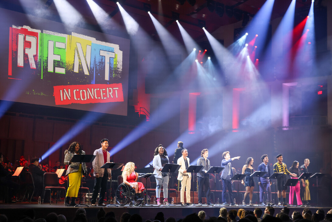 Twelve actors stand in a row with a symphony in the background.