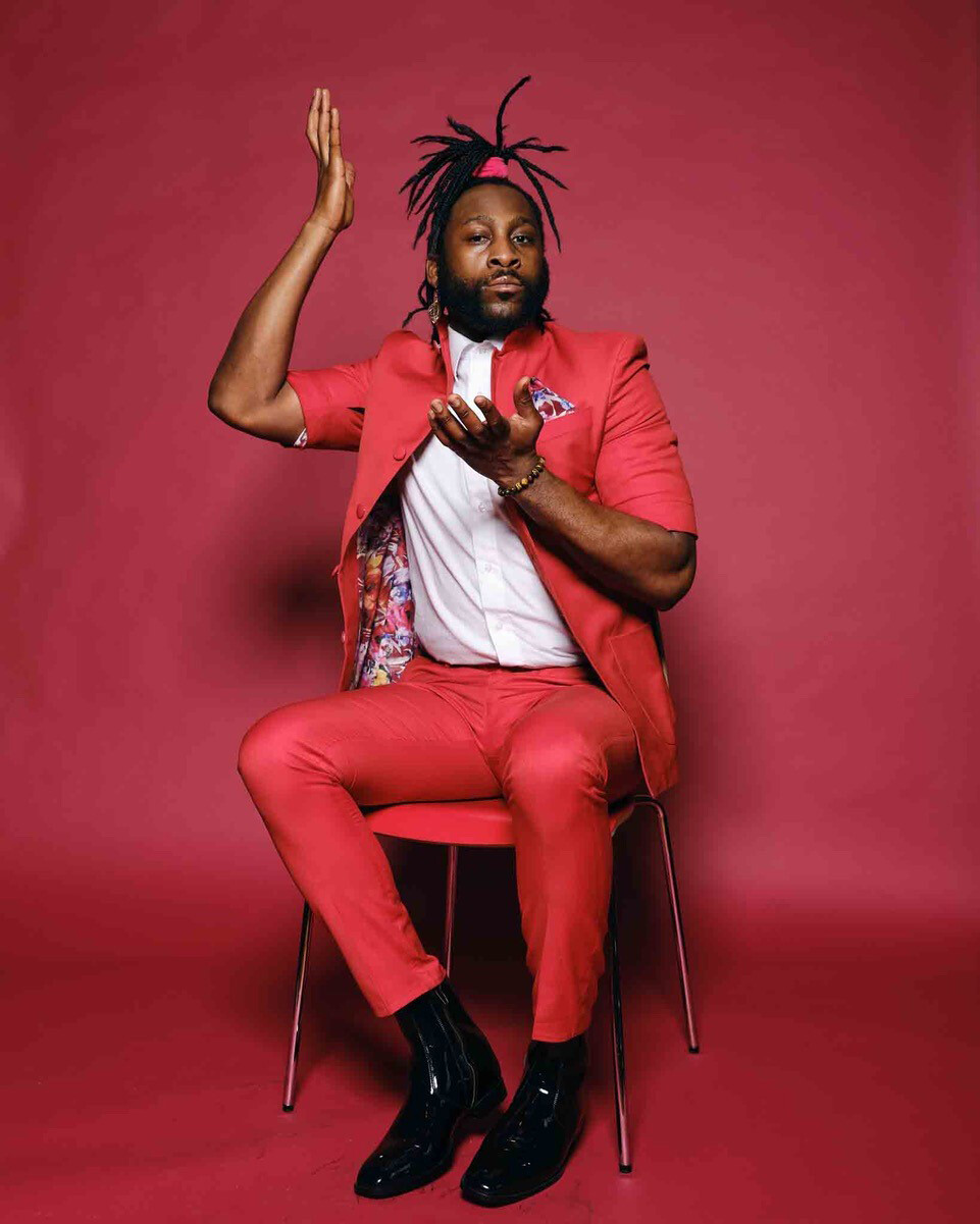 Portrait of Michael Mwenso, wearing a red suit, against a red background.