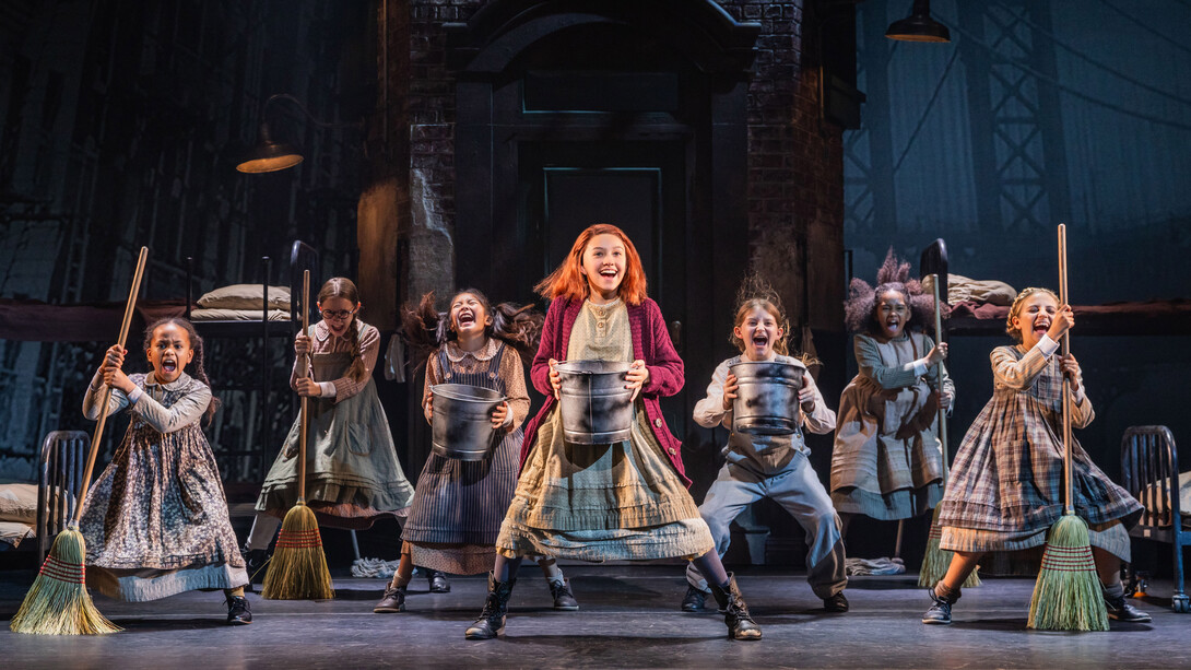 Seven young girls, dressed as orphans, dance with buckets and brooms onstage.